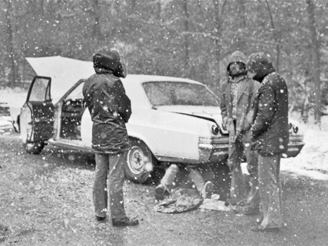 three men surround a broken-down 1965 Ford Fairlane in snowstorm while another attempts to fix it