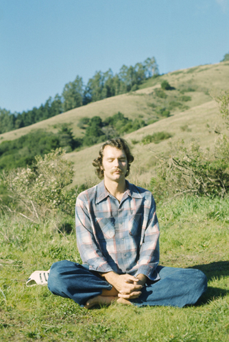 A man sits crossed-legged on a hillside in Marin County