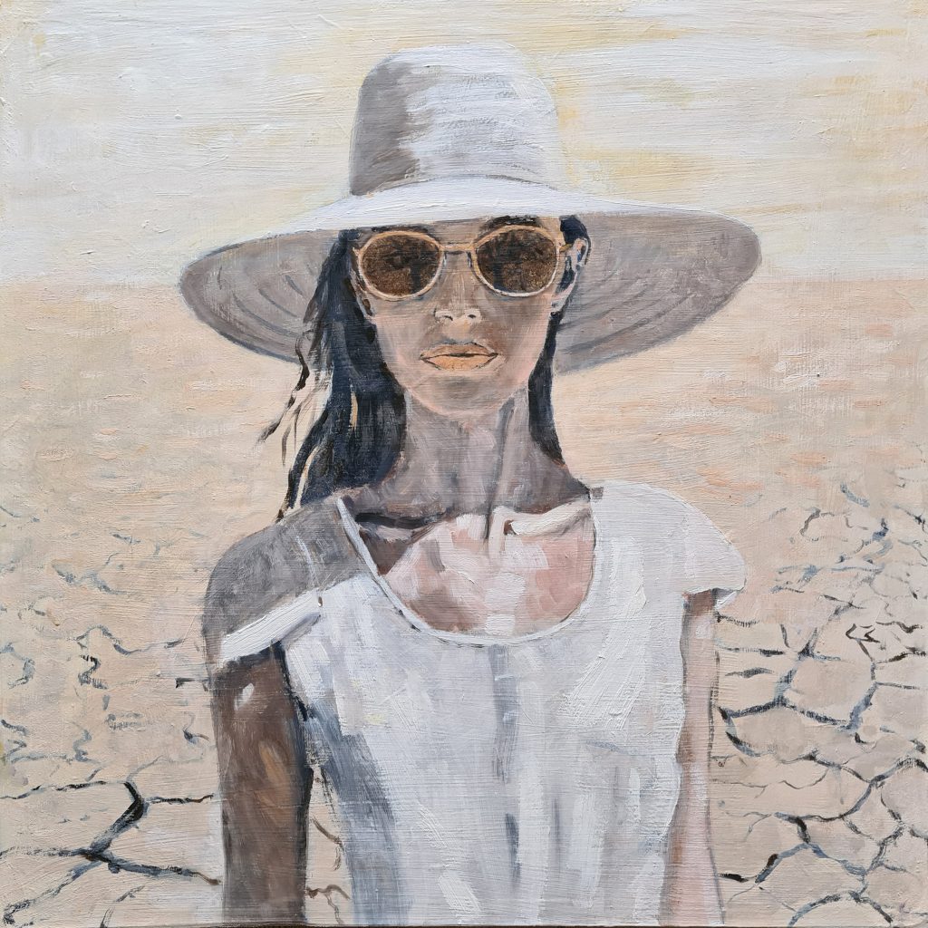 A woman wears a white hat and sunglasses as she stands in a desert